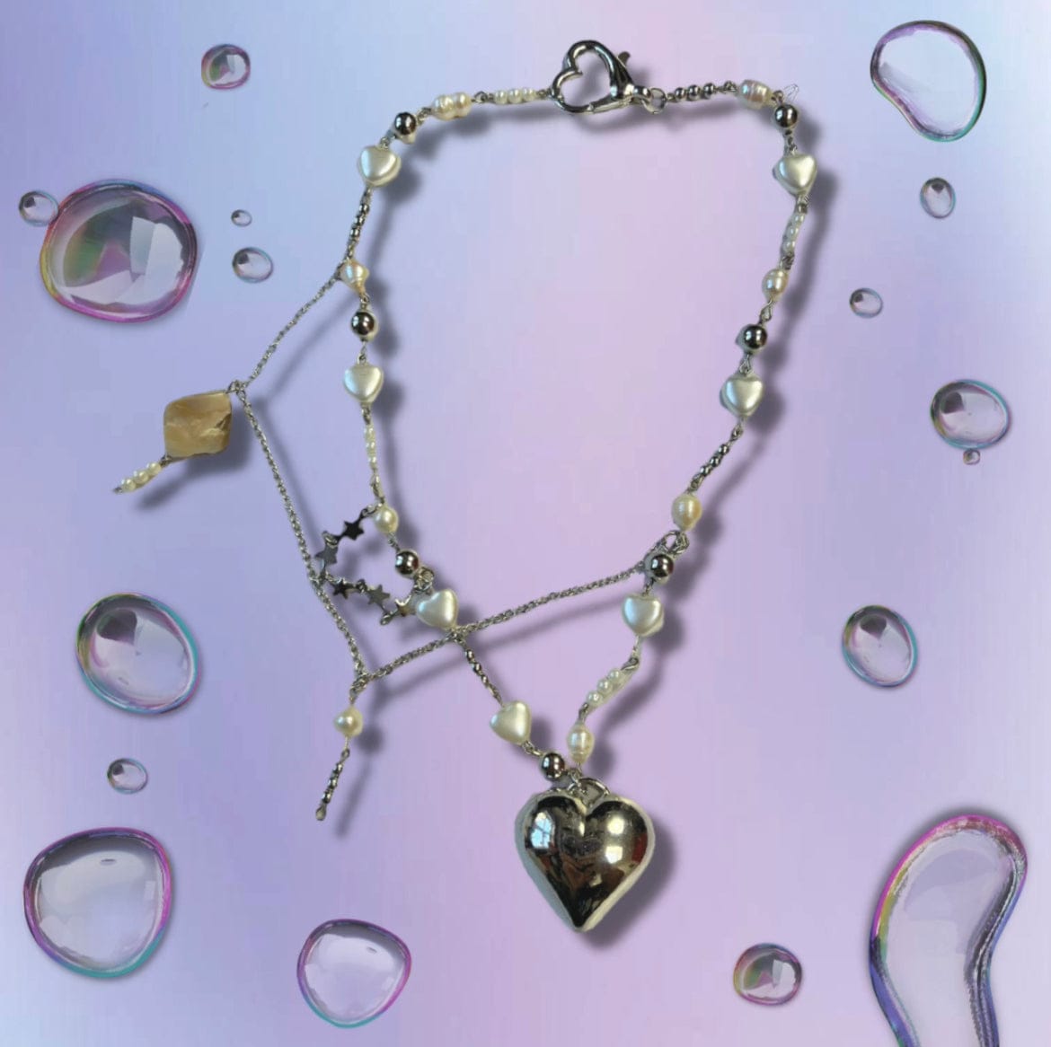 This 19 inch beaded necklace has pearl bubble hearts, pearl beads and silver balls. They are all connected by silver plated copper. Across the necklace is a chain with mother of pearl, pearls, and various silver and pearl beads. In between the layers there is a star chain. The pendant is a silver heart. Thé necklace is connected with a heart shaped clasp.
